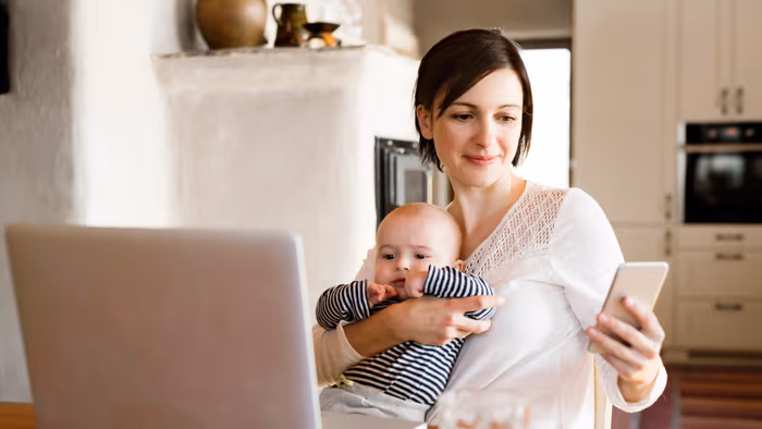 Em bé và mẹ ngồi trước máy tính xách tay, mỗi người cầm một chiếc điện thoại thông minh.