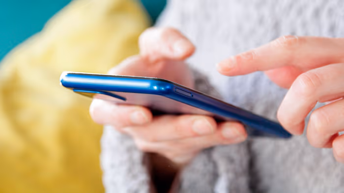 Cận cảnh một người mặc áo len xám đang sử dụng iPhone màu xanh dương.